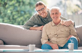 Happy, portrait and man with senior dad on sofa to relax together for fathers day, care or support. Smile, family and proud elderly male parent with person or son for bonding in living room in home